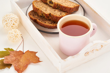 Autumn food-slices of banana bread, a Cup of tea, dry leaves, white wooden table. Cozy home winter. Side view, copy space