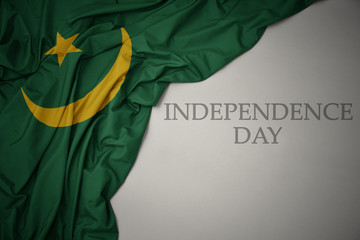 waving colorful national flag of mauritania on a gray background with text independence day.