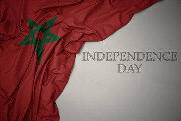 waving colorful national flag of morocco on a gray background with text independence day.