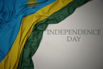waving colorful national flag of rwanda on a gray background with text independence day.