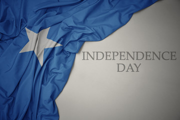 waving colorful national flag of somalia on a gray background with text independence day.
