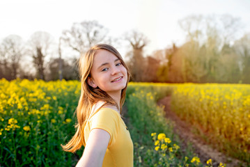 Young girl walking through yellow and green spring countryside fields