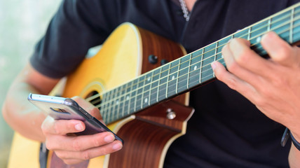 Fototapeta na wymiar Guitarist use smartphone in playing acoustic guitar time