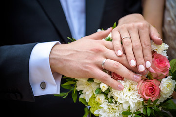 Obraz na płótnie Canvas Wedding pastel bouquet closeup in front of couple - groom and bride's hands with elegant manicure. Flowers lay on the dress with swan feather decor