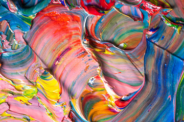 Different bright colors of oil paints are mixed on a palette close-up.