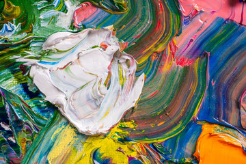 Different bright colors of oil paints are mixed on a palette close-up.