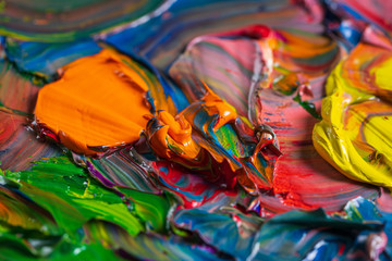 Different bright colors of oil paints are mixed on a palette close-up.