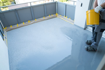 construction worker renovates balcony floor and spreads chip floor covering on resin and glue coating before applaying water sealant