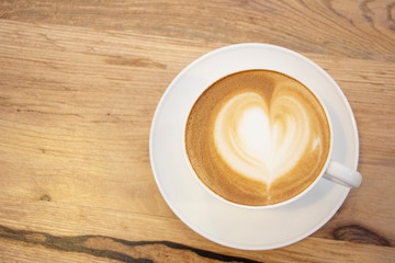 Heart-shaped foam coffee in white cup & saucer on wooden table 