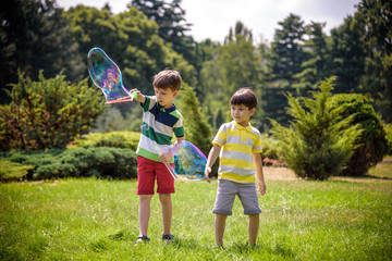 Fototapeta premium Boy blowing soap bubbles while an excited kid enjoys the bubbles. Happy teenage boy and his brother in a park enjoying making soap bubbles. Happy childhood friendship concept