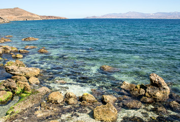 Fototapeta na wymiar Greece, the island of Paros. A view from the cliffs at the resort of Piso Livadi. Waves crash on the rocks. In the far distance, on the horizon, is the island of Naxos.