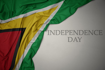 waving colorful national flag of guyana on a gray background with text independence day.