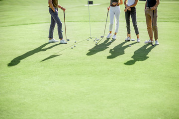 People practising golf, standing near the golf hall with balls and putters on a playing course outdoors, cropped image with shadows and no face