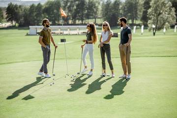 People practising golf, standing near the hall with balls and putters on a golf course outdoors