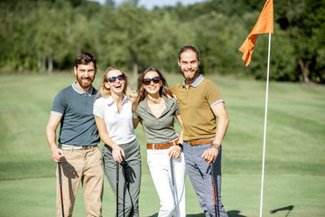 Portrait of a young and cheerful friends standing together near the golf flag on the playing course outdoors