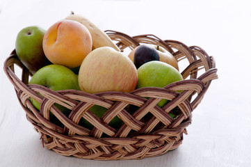 Apples, pears, plums, banana and peach in a wicker, brown basket on a light background. Fruit on a white background. Background of fruits.
