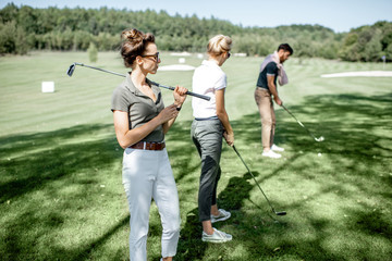 Portrait of an elegant young woman standing with golf putter and friends playing golf on the...