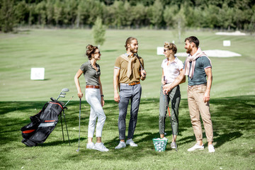Young and elegant friends standing together with golf equipment, having fun during a golf play on...
