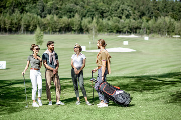 Obraz premium Young and elegant friends standing together with golf equipment, having fun during a golf play on the beautiful course on a sunny day