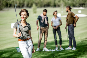 Portrait of an elegant young woman standing with golf putter and friends playing golf on the...