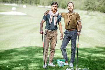 Portrait of a two male best friends standing with playing equipment on a golf course, hanging out together during a game on a sunny day