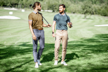 Two male best friends walking with golf equipment on beautiful playing course, talking and having fun during a game on a sunny day
