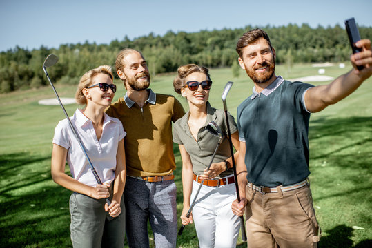 Group of young and happy friends making selfie photo while standing together with golf putters during a game on the golf course