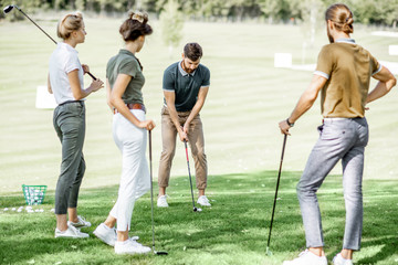 Group of a young people dressed casually playing golf on the beautiful golf course on a sunny day,...