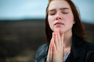 Red-haired girl prays with closed eyes