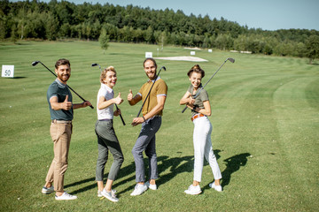 Portrait of a young group of friends walking with golf equipment on the beautiful golf course...
