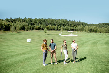 Fototapeta premium Portrait of a young group of friends standing with golf equipment on the golf course during a game on a sunny day, wide landscape view
