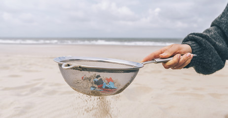 Young woman cleaning microplastics from sand on the beach, Environmental problem, pollution, ecolosystem and climate change warning concept 