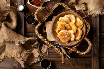 overhead breakfast shot with tasty fried russian pancakes with powdered sugar on top in wooden bowl stands in wicker straw basket with forks on rustic brown table