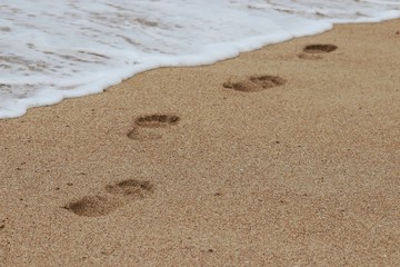 Bare footprints in the sand and a sea foaming wave running on the shore. Beach holidays, concept of freedom, happiness and romance