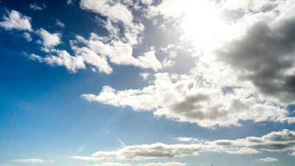 Obraz premium Sun breaking through white clouds with vibrant blue sky background taken on a warm spring/summer day.