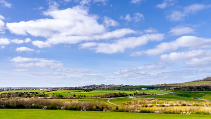 Fototapeta na wymiar Scenic landscape view showing parts of Herrington Country Park in Sunderland Tyne and Wear. Panorama features blue sky, clean white clouds and lush green fields on a warm sunny day.