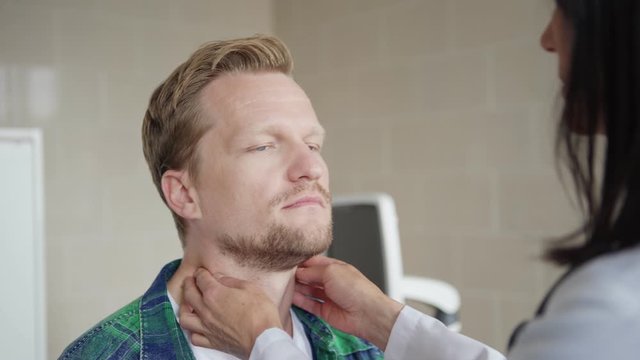 Closeup of female general practitioner checking lymph nodes or tonsils of middle aged male patient in doctors office