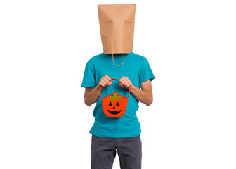 Happy halloween concept. Teen boy with paper bag over his head holds orange pumpkin bucket, isolated on white background. Portrait of teenager cover head with bag. Child waiting candy.