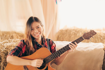 Music Concepts. Asian Caucasian girl in countryside playing guitar. Asian women relaxing with music. Asian women have a happy lifestyle.