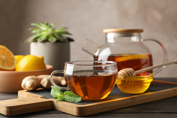 Cup of tea, mint, honey, ginger and teapot on wooden background, space for text