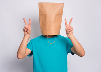 Portrait of teen boy with paper bag over head making Victory gesture. Teenager cover head with bag showing victory sign posing in studio. Child pulling paper bag over head.