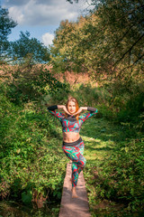 Young beautiful slim woman in sportswear is engaged in fitness yoga outdoors in the forest.