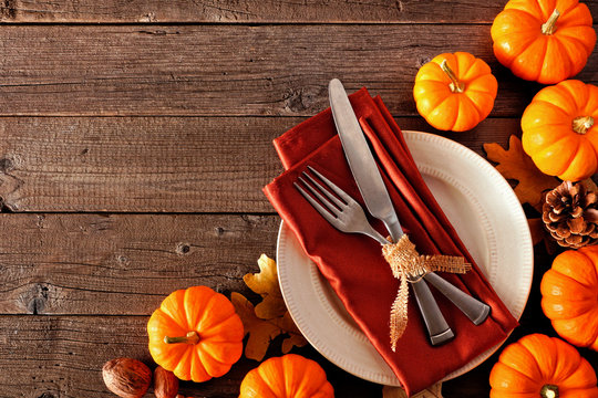 Thanksgiving table setting with fork and knife on a plate with orange napkin and pumpkin border against a rustic wood background