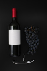 Bottle of red wine with label, corkscrew  and ripe grapes