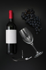 Bottle of red wine with label with glass and ripe grapes on black