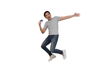 Excited Asian young man in gray t-shirt jumping and holding credit card isolated over white background, Full length portrait concept