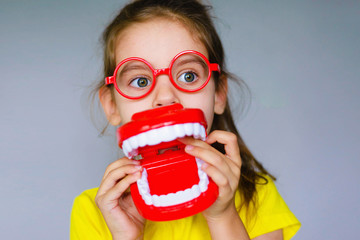 Little funny girl kid with toothbrush, dental mockup (jaw), red glasses in hand. Concept of health,...
