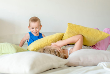 Little boy and his older sister having fun while fighting with pillows in the bedroom