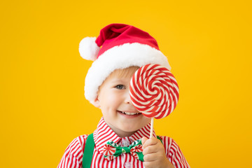 Happy child holding lollipop in hand against yellow background