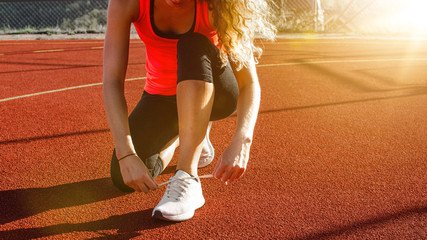 junge hübsche Frau mit lockigem Haar kniet auf Hartplatz um ihre Schuhe vor dem Joggen zu binden